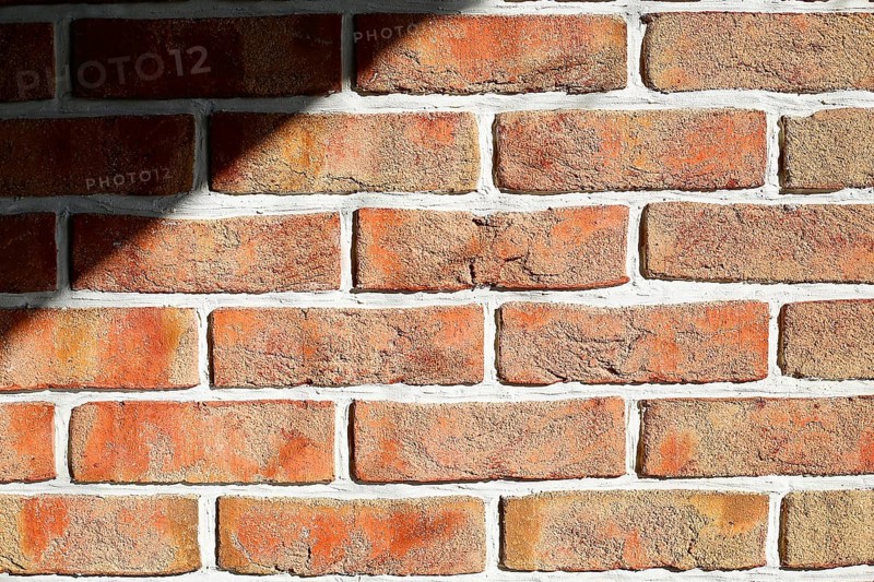 Sunlight and shadow on a textured red brick wall with white mortar, background image