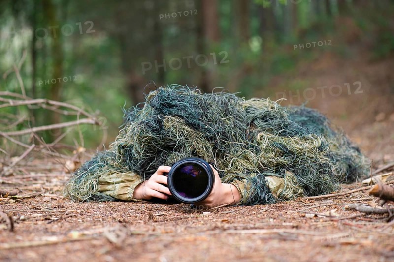 Photographer wearing camouflage clothing in the forest, wildlife animal photography with a camera and telephoto lens