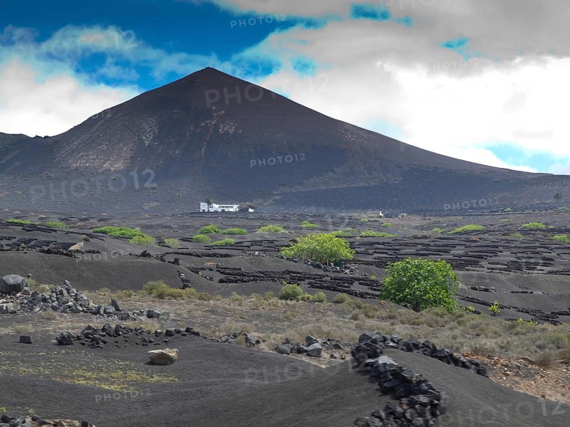 A volcano with black soil, green trees and clouds in the sky, arrecife, Lanzarote, Canary Islands, Spain, Europe