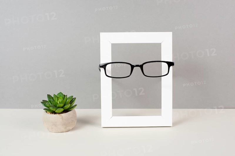 Home interior poster mock up with wooden frame, eyeglasses and cactus in a pot, gray wall background, copy space for text and pictures