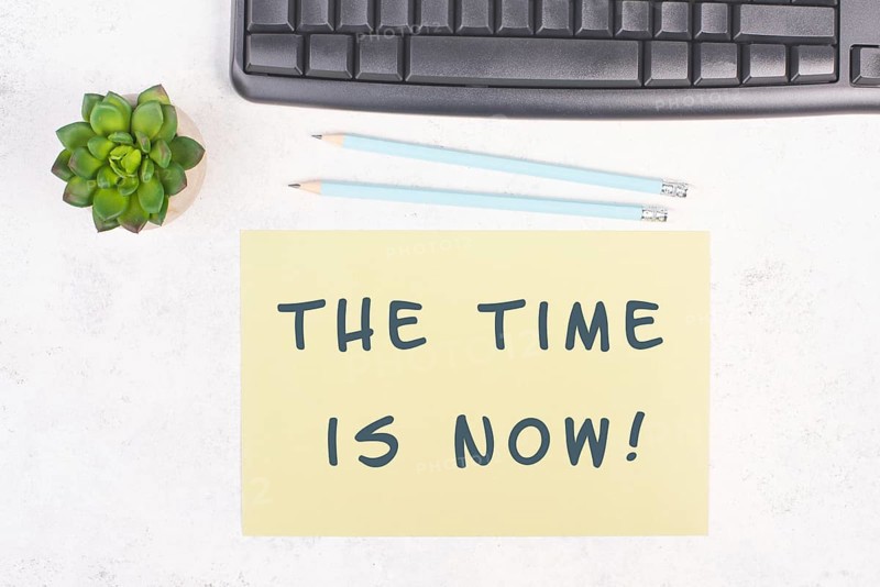 The phrase the time is now is standing on a paper, a pen, computer keyboard and a cactus, brainstorming for new business ideas, startup concept, home office desk