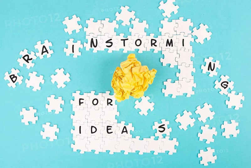 Puzzle on a blue background, yellow crumpled paper, words brainstorming for ideas are standing on the jigsaw pieces, business concept, working as a team together