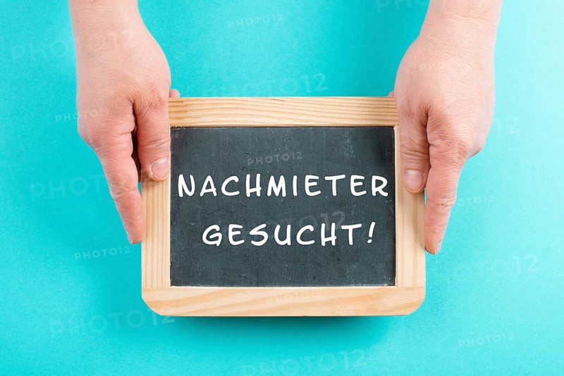 Holding a chalkboard in the hands, looking for a new tenant is standing in german language on the sign, moving to a new home, real estate