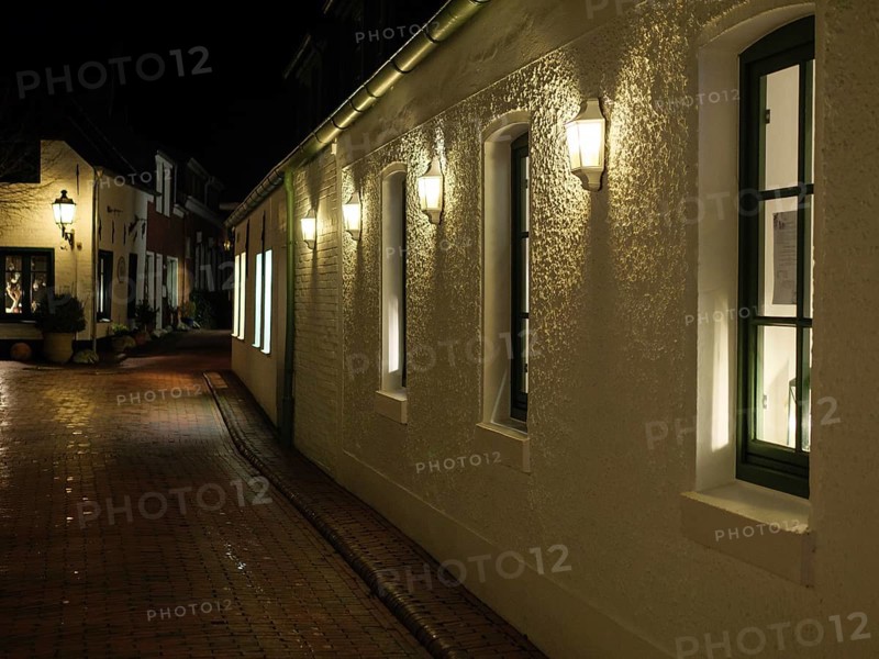 A dark street at night with white, illuminated buildings and cobblestones under streetlights, greetsiel, east frisia, germany