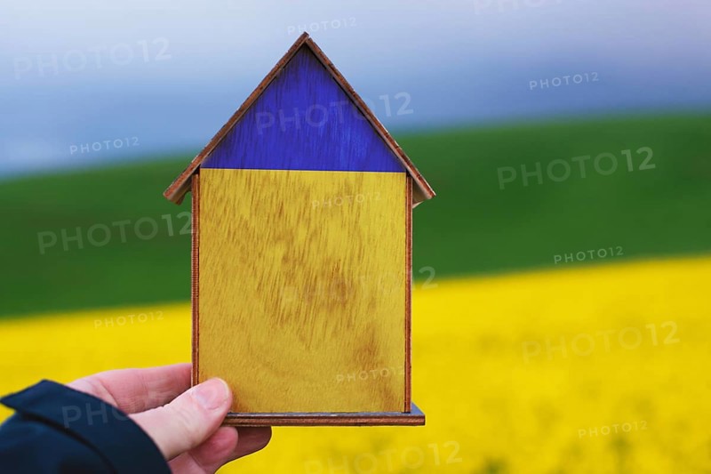 Holding a house in the hand with the colors of the ukrainian flag, home for refugees from Ukraine, help for families