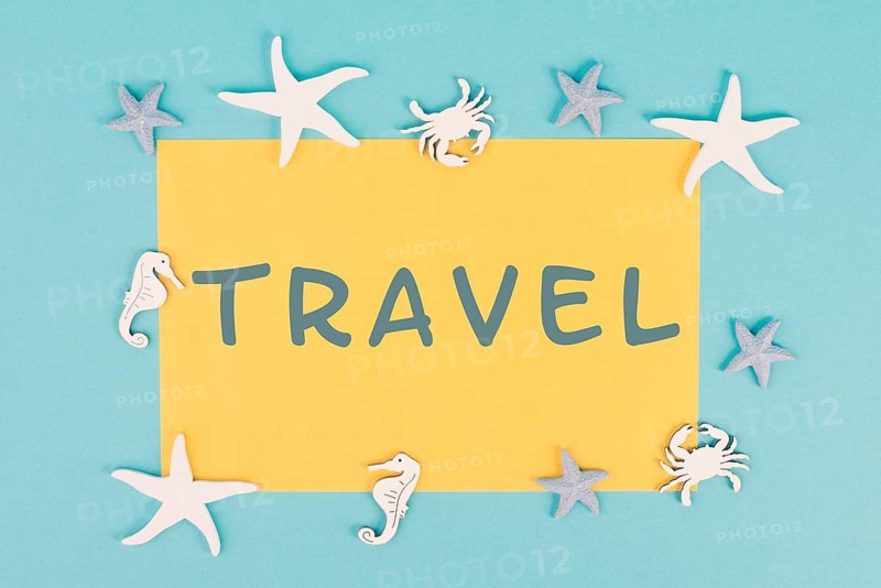 The word travel is standing on a yellow colored paper, sea stars, seahorses and crab bulding a frame, summer vacation, tourism destination