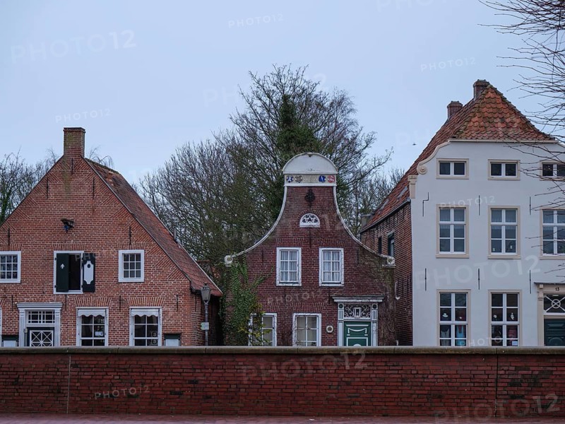 Three historic house fronts with brick facades in front of a cloudy sky, greetsiel, east frisia, germany