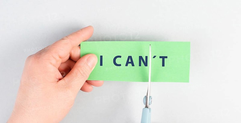 The word can not is standing on a paper, cutting the not with scissors, having a goal, postive thinking, be an optimist, do it, self confident