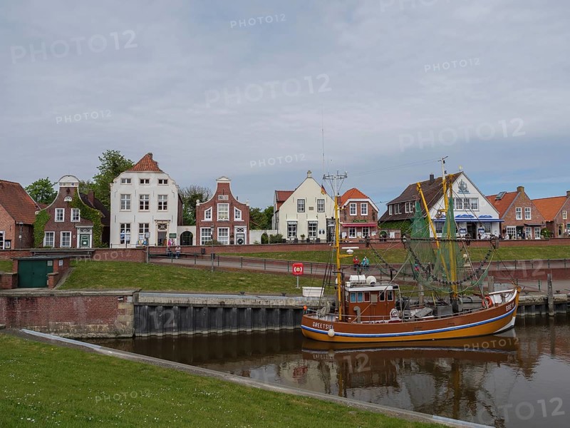 Houses line the harbour where a fishing boat is anchored in the calm water, Greetsiel, East Frisia, Lower Saxony, Germany, Europe