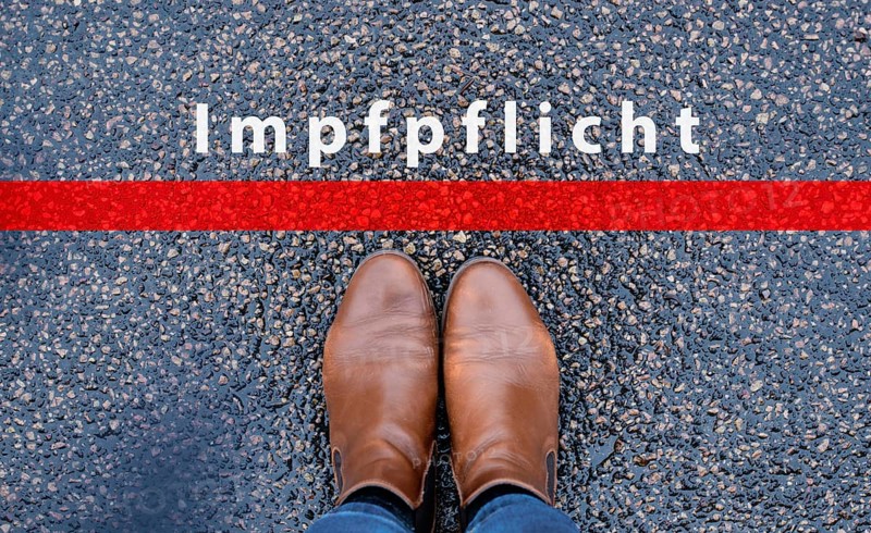 The word mandatory vaccination is standing on the road, german language, compulsary vaccine, covid-19 regulations, red line in front of shoes