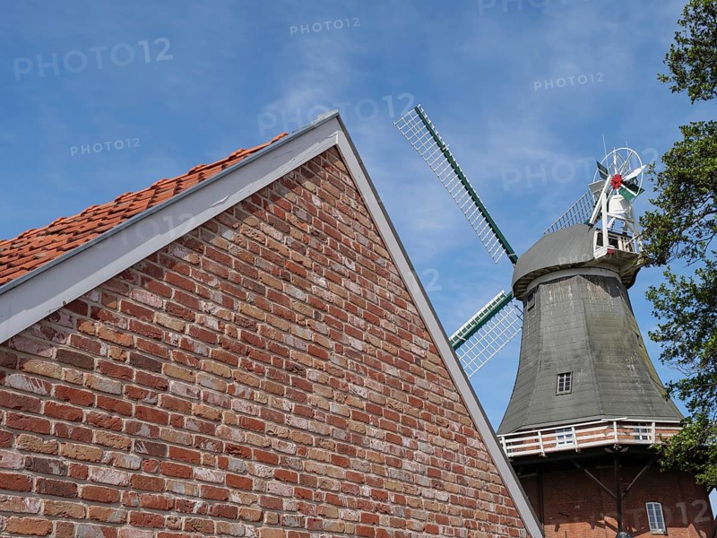 Brick building with the top of a windmill in the background under a blue sky, Greetsiel, East Frisia, Lower Saxony, Germany, Europe