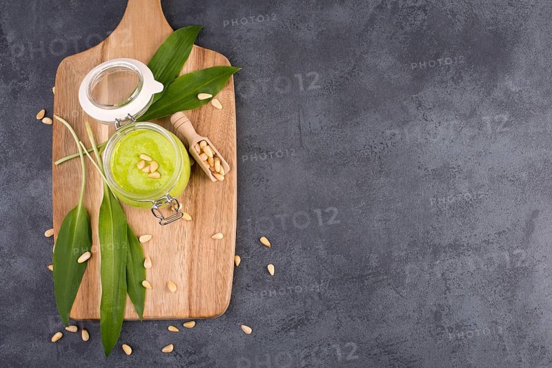 Pesto made from wild garlic, pine nuts and feta cheese in a glass, with fresh leaves on a dark textured background, empty space for text