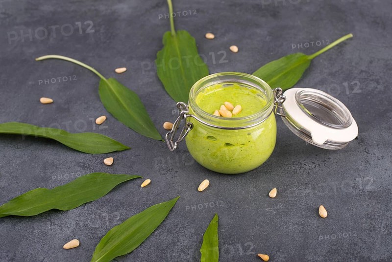 Pesto made from wild garlic, pine nuts and feta cheese in a glass, with fresh leaves on a dark textured background, empty space for text
