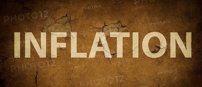 The word inflation is standing on a brown textured wall, increasing living costs