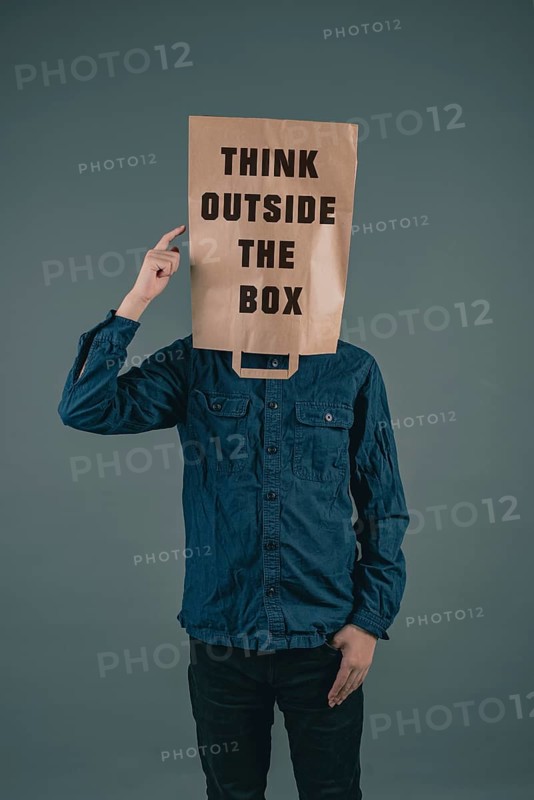 Young men has a paper bag on his head, the phrase think outside the box is standing on it, brainstorming for new ideas, be innovative