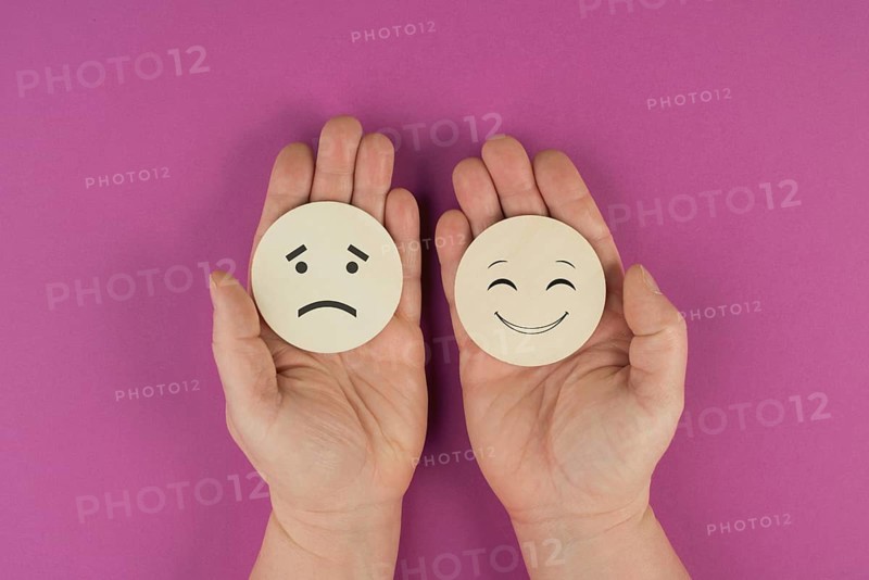 Holding two wooden circles in the hands one face is sad the other one is smiling, positive and negative emotions, rating concept, choosing the mood