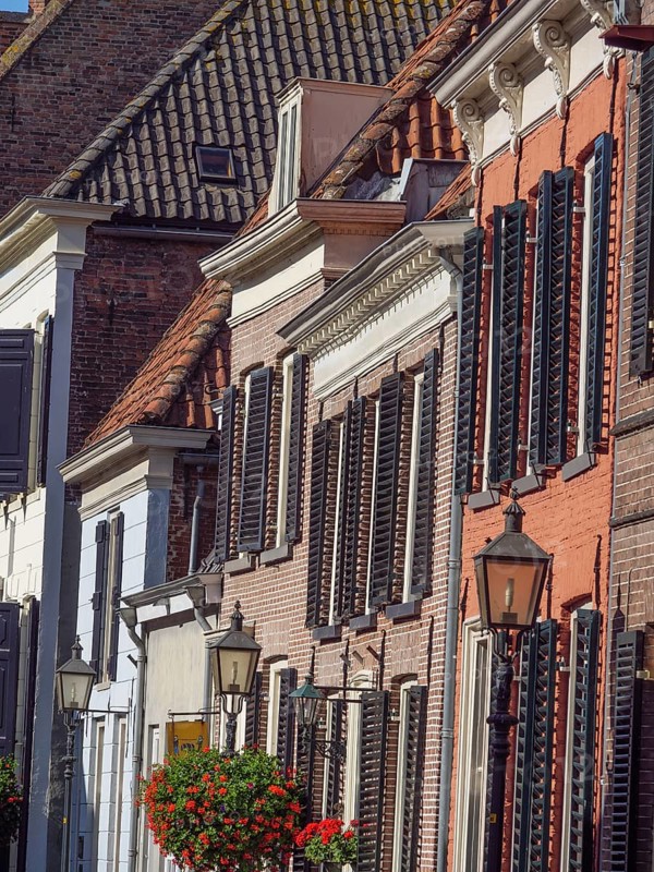 Row of historic brick houses with white lattice windows, lanterns and red flower pots in traditional Dutch style on a sunny day, Doesburg, Gelderland, Netherlands