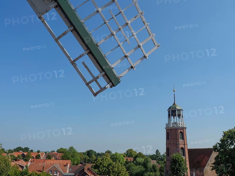 Parts of a windmill and a church tower rise above the roofs of a quiet village, Ditzum, rheiderland, Lower Saxony, Germany, Europe