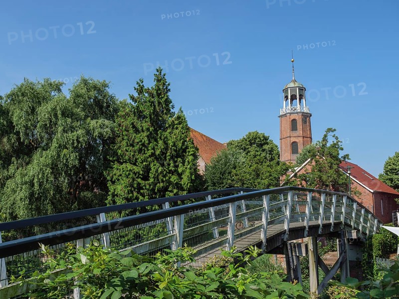 Wooden bridge leading to a church tower, surrounded by lush green vegetation and blue sky, Ditzum, rheiderland, Lower Saxony, Germany, Europe