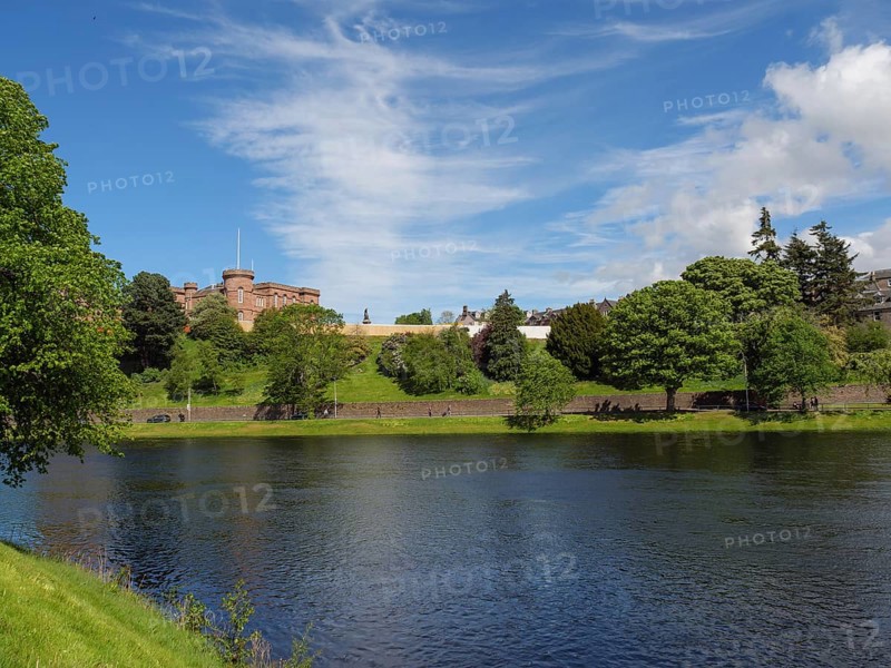 A river flows in front of a green hill and a castle, surrounded by lush vegetation and a clear sky, inverness, scotland, United Kingdom, Europe