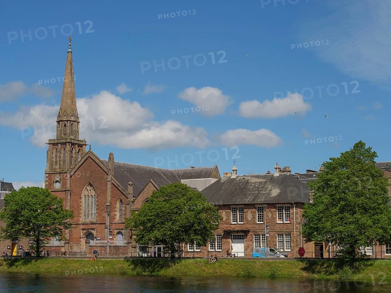 Church tower and urban buildings along a river with trees and blue sky with clouds, inverness, scotland, Great Britain