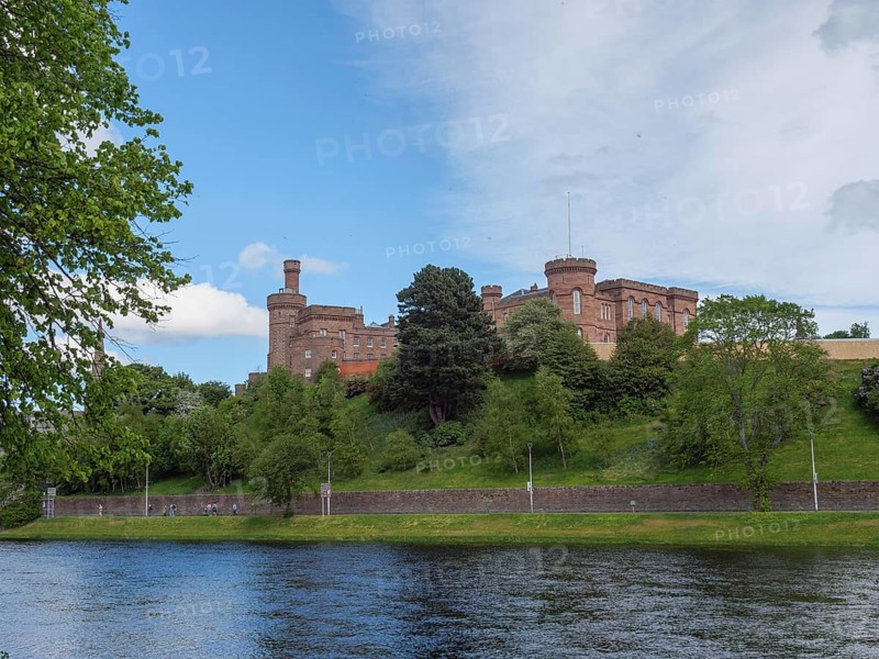 A castle overlooking a river, surrounded by green banks and trees under a blue sky, inverness, scotland, Great Britain