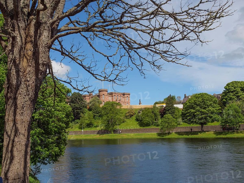 A castle on a hill on the banks of a river, surrounded by trees and under a blue sky, inverness, scotland, Great Britain