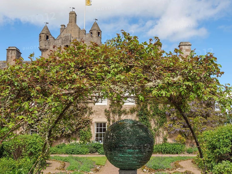 Castle with towers in the background, an archway of plants and a sculpture in a well-tended garden, inverness, scotland, Great Britain