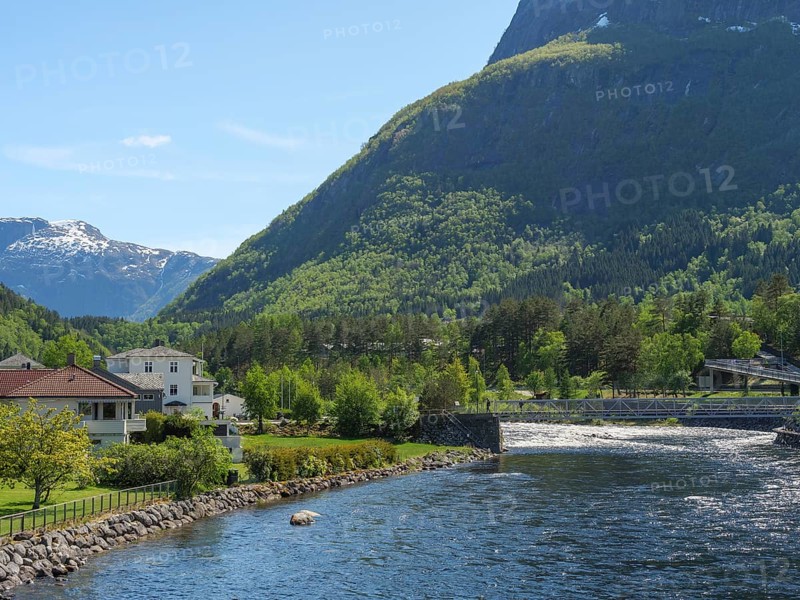 A river with a bridge, flanked by houses and trees, embedded in a green valley with mountains in the background, Eidfjörd, Norway, Scandinavia, Europe