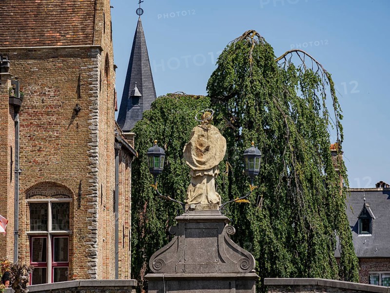 Statue in the foreground in front of historic brick buildings, a church with spire and gardens, Bruges, Flanders, Belgium, Europe