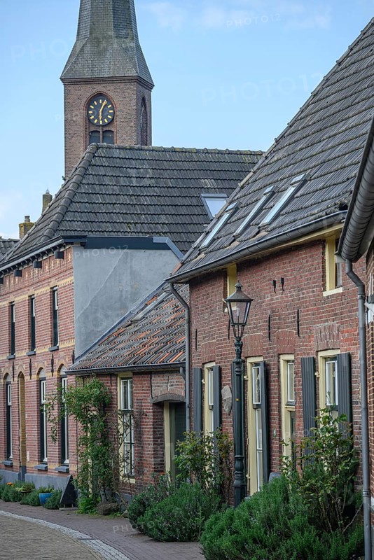A peaceful village street with a view of the church tower, surrounded by old brick houses, planted front gardens and shutters, Bredevoort, gelderlande, the netherlands
