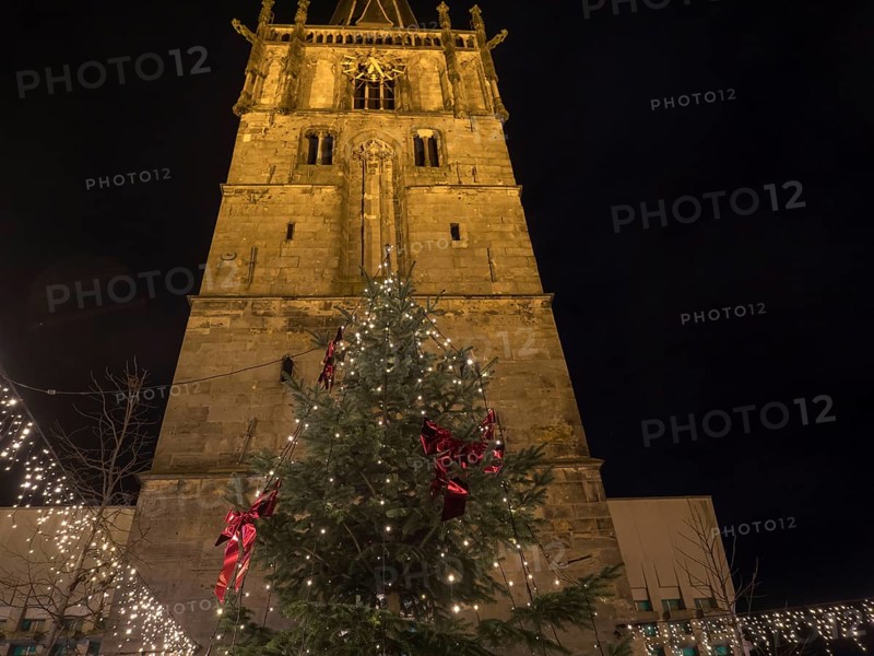 A tall church tower with a festively decorated Christmas tree full of fairy lights below, all at night, Ahaus, Münsterland, North Rhine-Westphalia, Germany, Europe