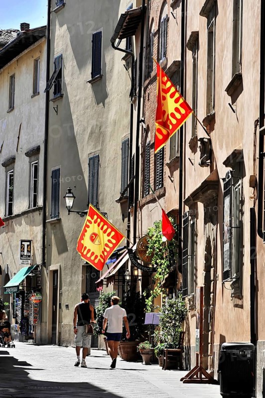 Volterra, Tuscany, Italy, Europe, Colourful historic street with flags and two men walking, sunny weather, ancient charm, Europe