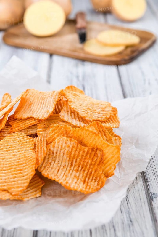 Bowl with rippled Potato Chips (selective focus) on wooden background