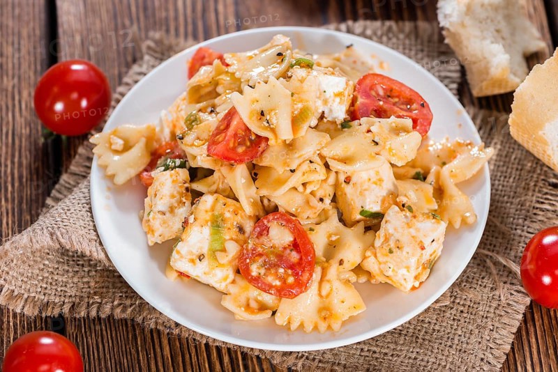 Portion of Pasta Salad with Farfalle, Cheese and Tomatoes (on wooden background)