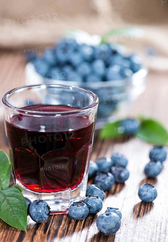 Blueberry Liqueur in a shot glass (on wooden background)