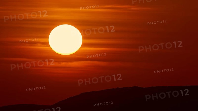 A large, bright ball of sunlight in the sky sinks behind the dark silhouettes of hills, offshore island, Kritinia Castle, St John's Castle, Kritinia, Rhodes, Dodecanese, Greek Islands, Greece, Europe