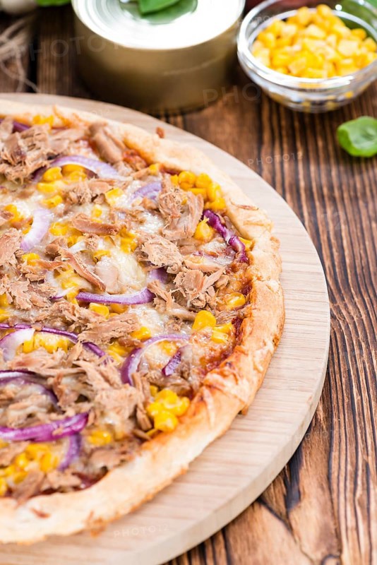 Fresh made Tuna Pizza (close-up shot) on rustic wooden background