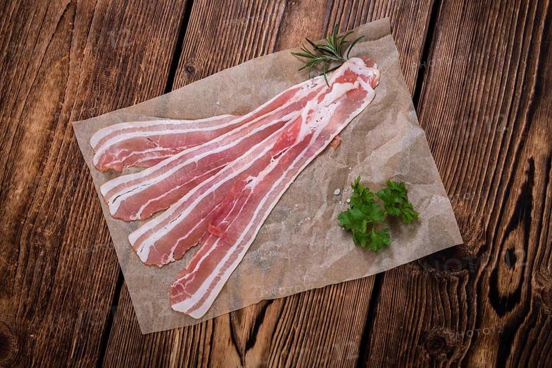 Portion of raw Bacon (close-up shot) on wooden background