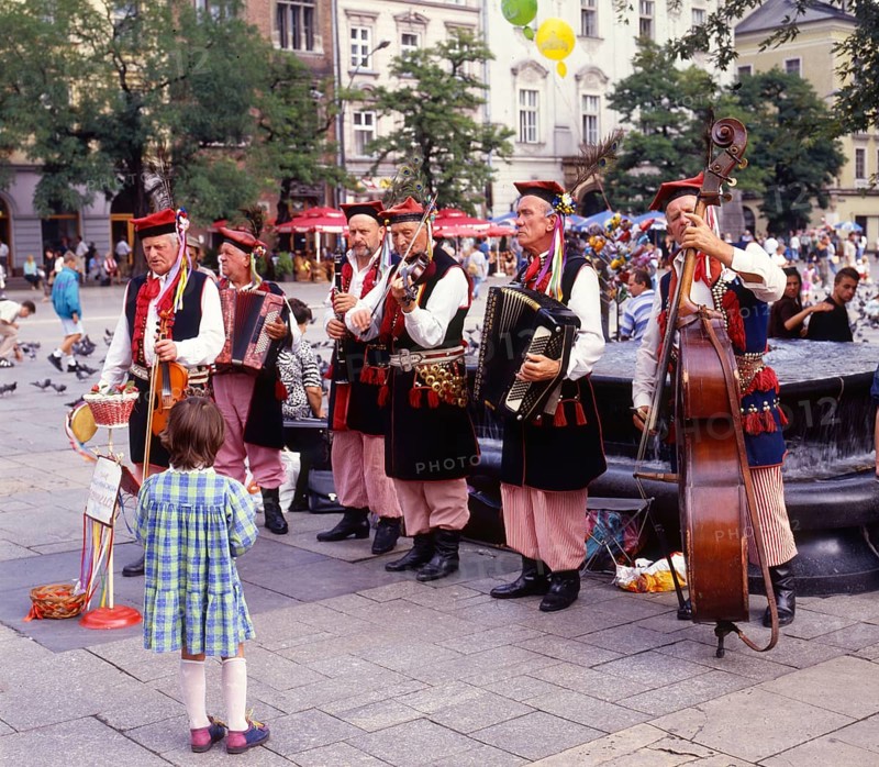 Little girl listens to music band of elderly men dressed in Polish national costumes in a square in Krakow, Poland, Europe. Scanned 6x6 slide, Europe