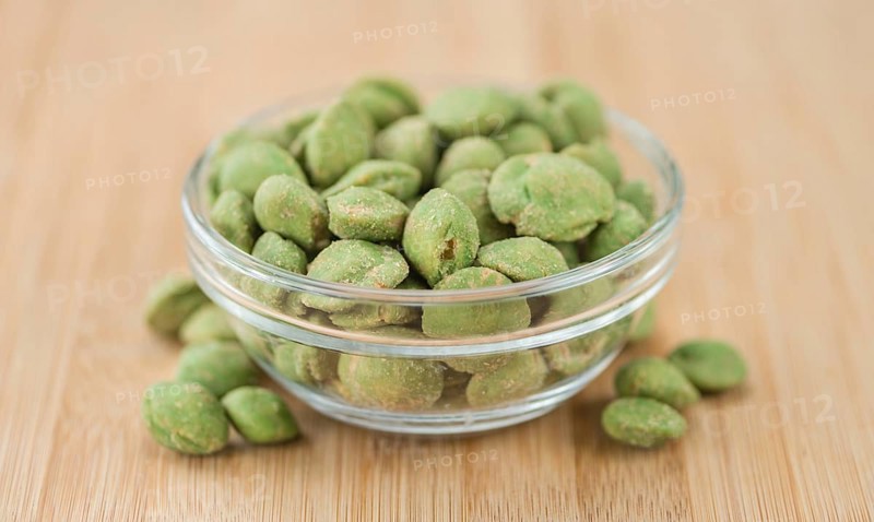 Wasabi coated Peanuts as high detailed close-up shot on a vintage wooden table (selective focus)