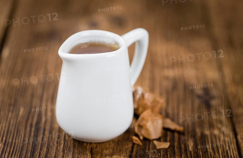 Caramel Syrup as high detailed close-up shot on a vintage wooden table (selective focus)