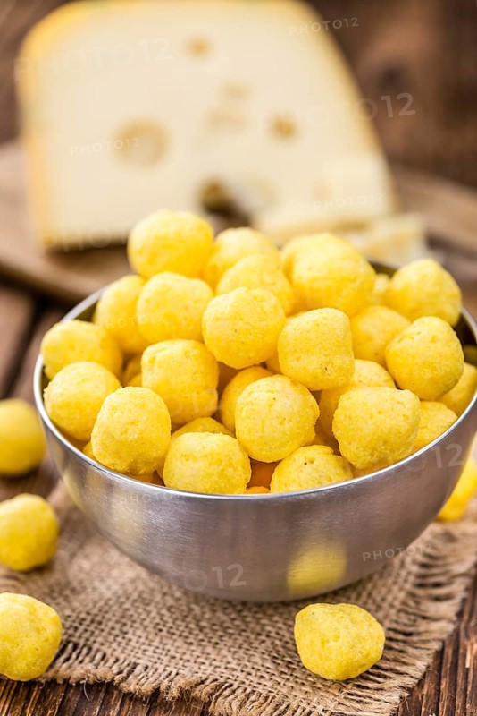 Cheese Balls (fried) as high detailed close-up shot on a vintage wooden table (selective focus)