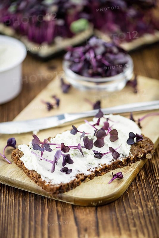 An old wooden table with healthy food (slice of bread, cream cheese and fresh cutted cress), selective focus