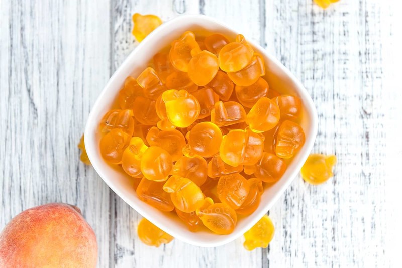 Gummy Peaches (close-up shot) with some fresh fruits on wooden background