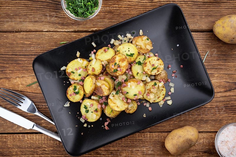 Fried Potatoes with Onions ond ham on a wooden table (selective focus)