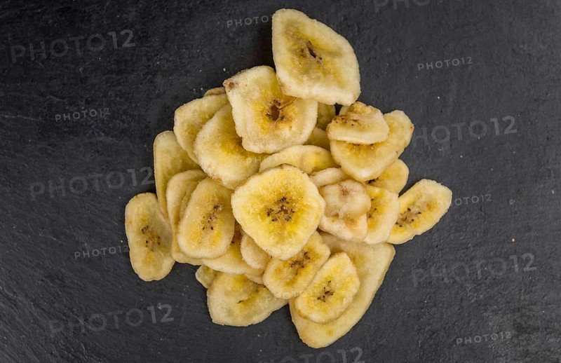 Some Dried Banana Chips on a slate slab as detailed close-up shot, selective focus
