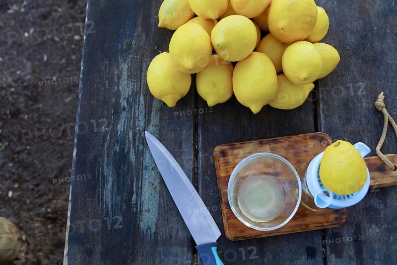 Top view of a lemon squeezed with a hand juicer on a wooden table with a knife and a pile of lemons beside it