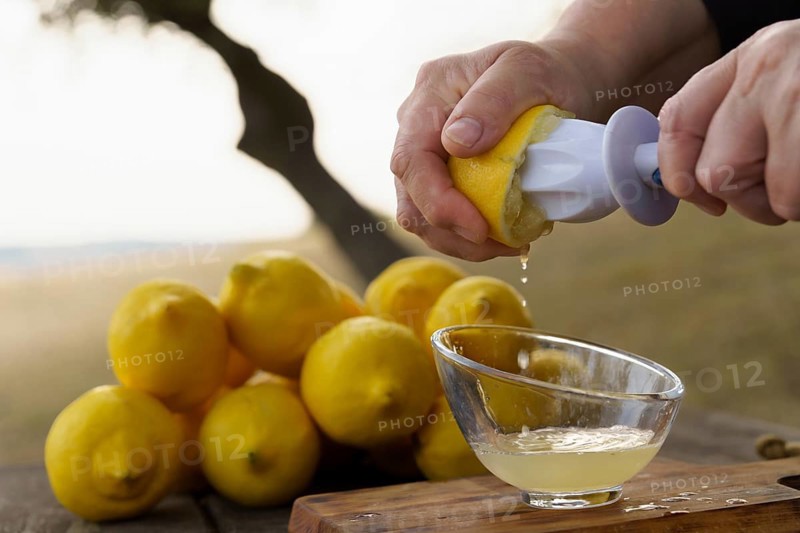 Close-up of a woman's hand squeezing a lemon in a hand juicer on a wooden table in the field