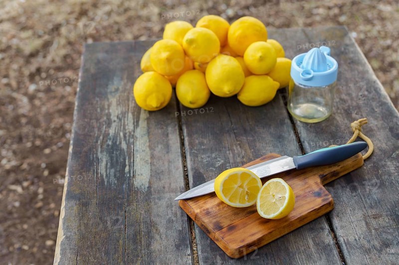 Top view of a lemon cut with a knife on a wooden board in the background pile of lemons and a juicer